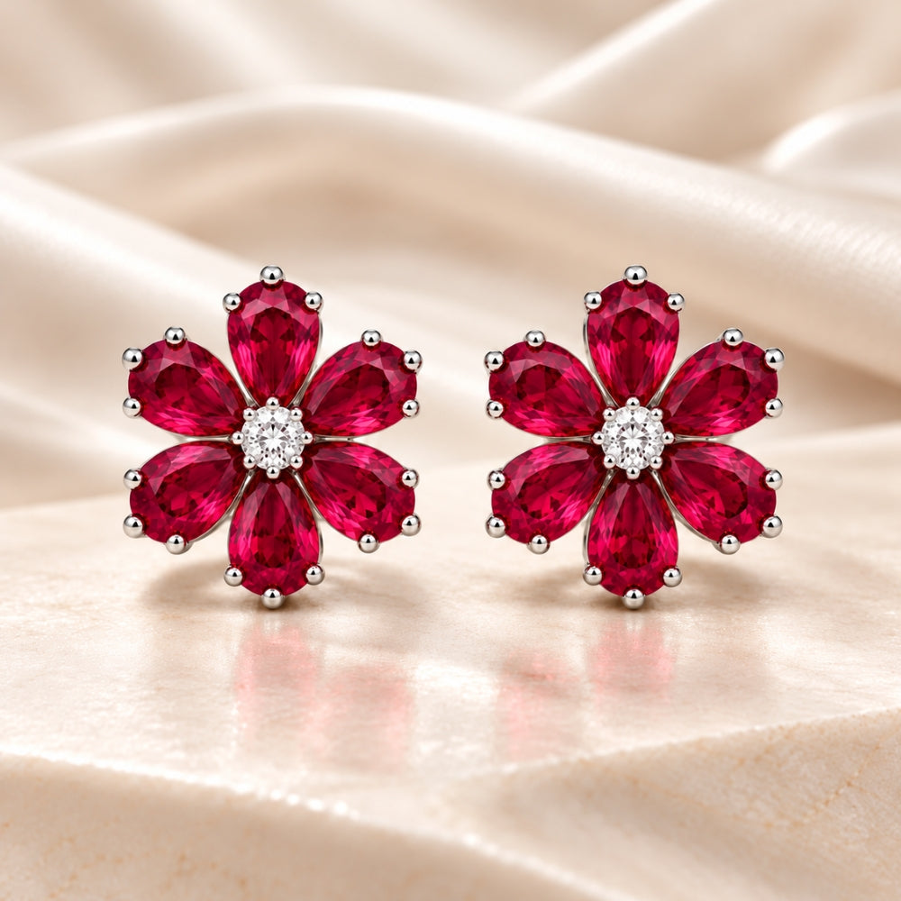 MARLA Fine Jewellery floral stud earrings featuring six ruby-red pear-shaped gemstones, sparkling round centre stones and polished silver-tone settings on cream marble.