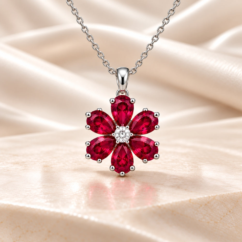 Elegant MARLA Fine Jewellery silver-tone necklace featuring a floral pendant with six ruby-red pear-shaped gemstones and a sparkling round centre stone on cream satin.  Copy