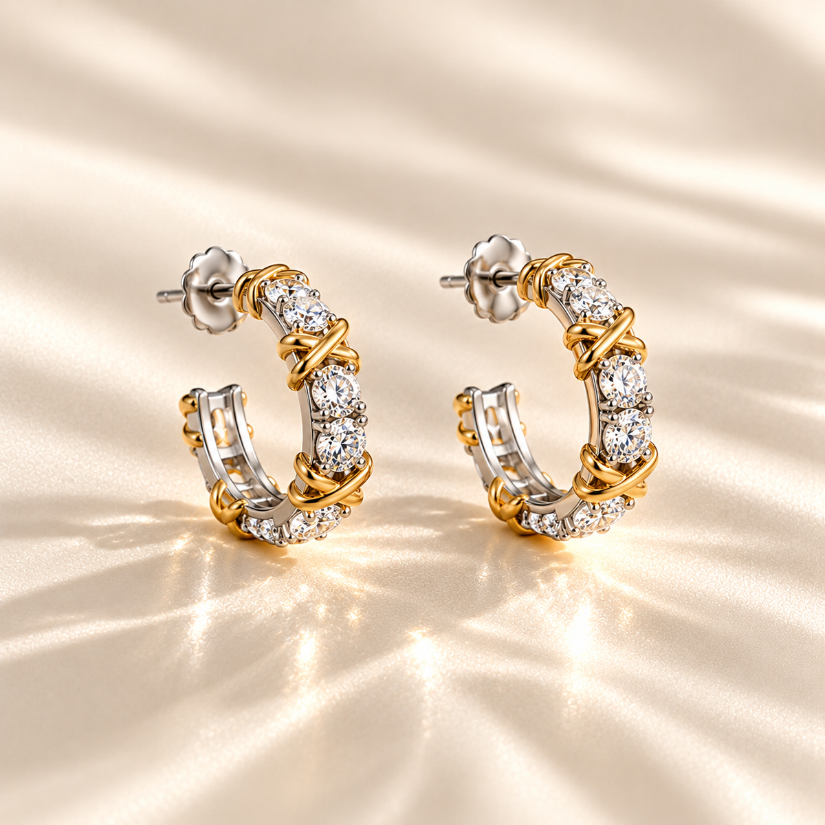 MARLA Celia Earrings featuring sparkling moissanite stones set in sterling silver with elegant gold X-shaped accents, displayed on a luxurious champagne satin background.
