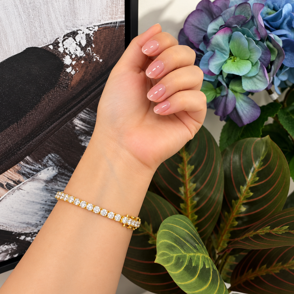MARLA gold moissanite tennis bracelet worn on a model's wrist with pink manicure and elegant floral background
