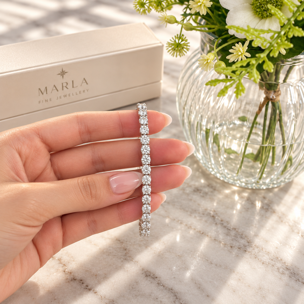 MARLA silver 4mm moissanite tennis bracelet with round brilliant stones held by a model's hand beside luxury jewelry packaging