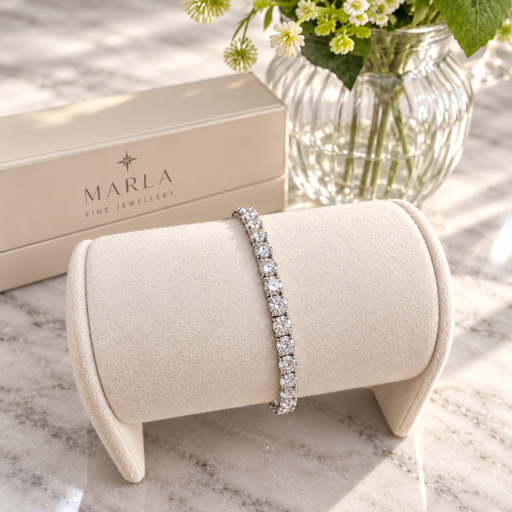 MARLA silver 4mm moissanite tennis bracelet displayed on a cream velvet jewelry stand with elegant floral background
