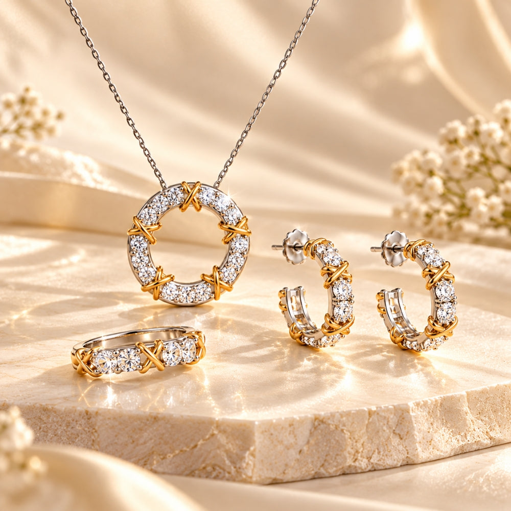 MARLA Celia Jewellery Set featuring a moissanite pendant necklace, matching hoop earrings and ring with gold crisscross details, elegantly displayed on a cream stone platform with soft floral accents.