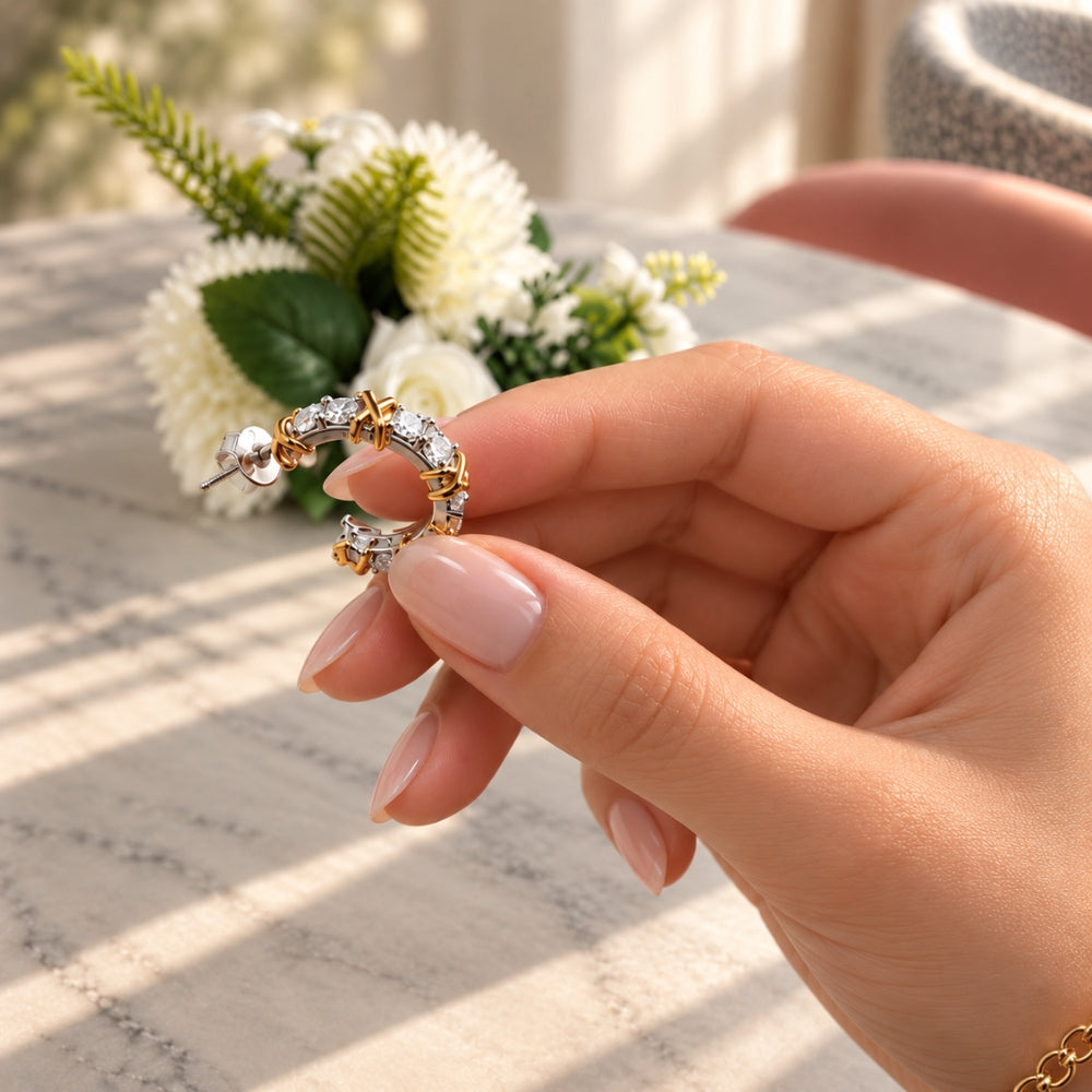 Close-up of a Celia Moissanite Hoop Earring held by a model, highlighting the sparkling stones, polished sterling silver and gold crossover accents.