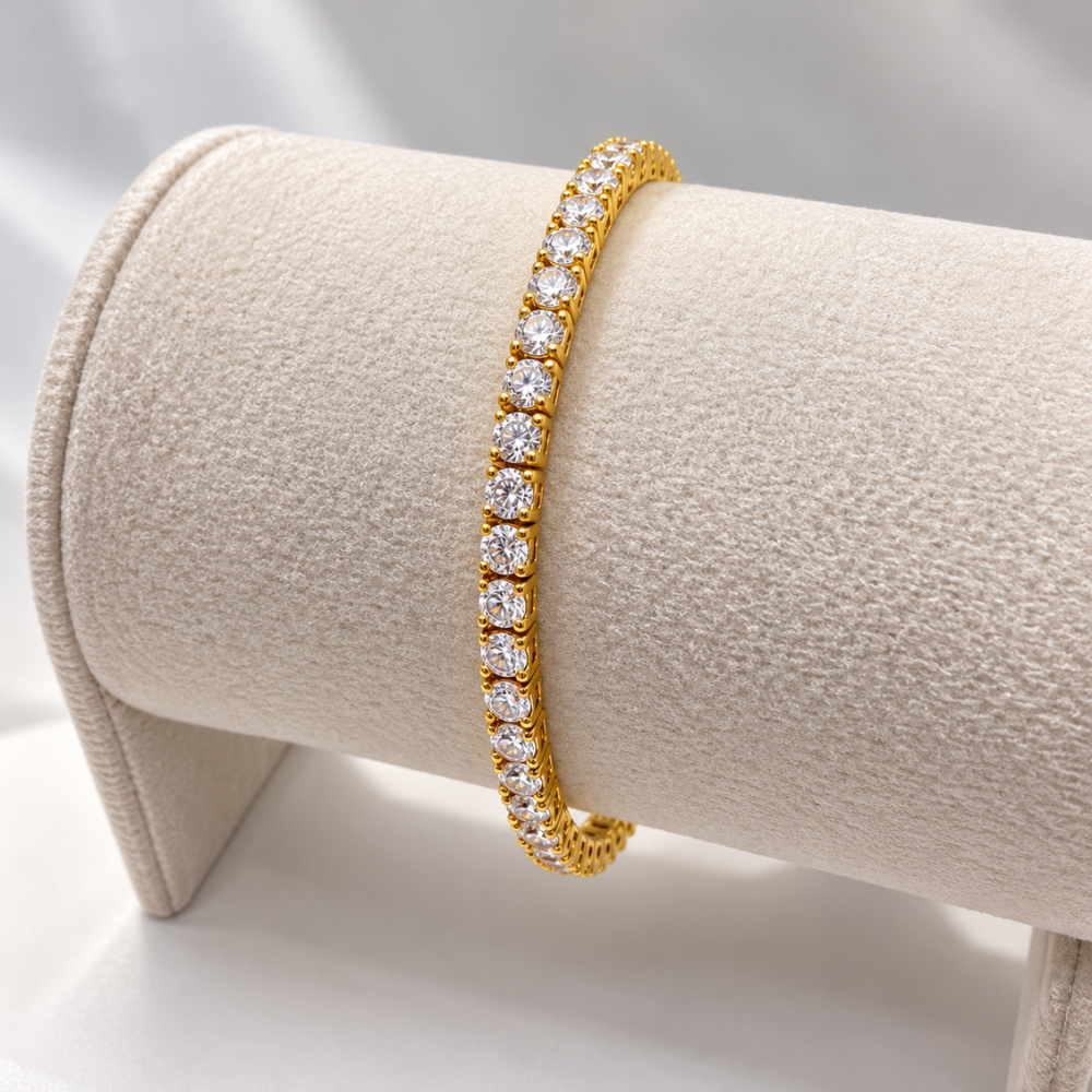 MARLA gold-tone tennis bracelet with sparkling round moissanite stones displayed on a luxurious cream velvet jewellery stand.