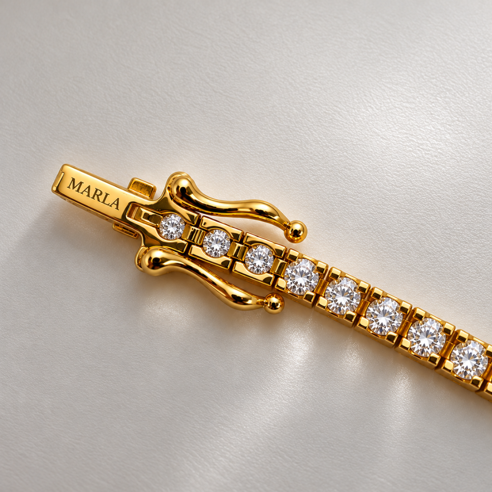 Close-up of MARLA gold-tone tennis bracelet featuring round moissanite stones, a secure safety clasp and engraved MARLA branding.