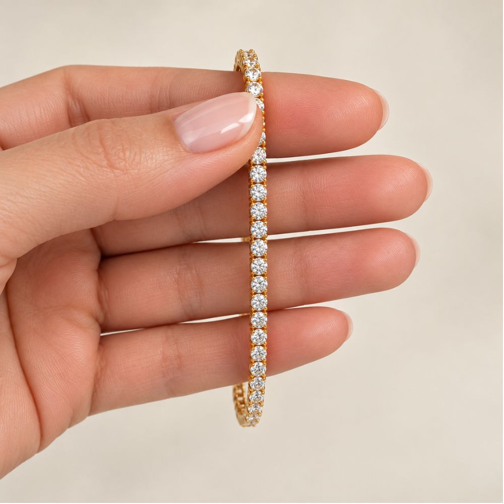 Gold 3mm moissanite tennis bracelet held between a model's fingers, highlighting sparkling stones and gold setting.