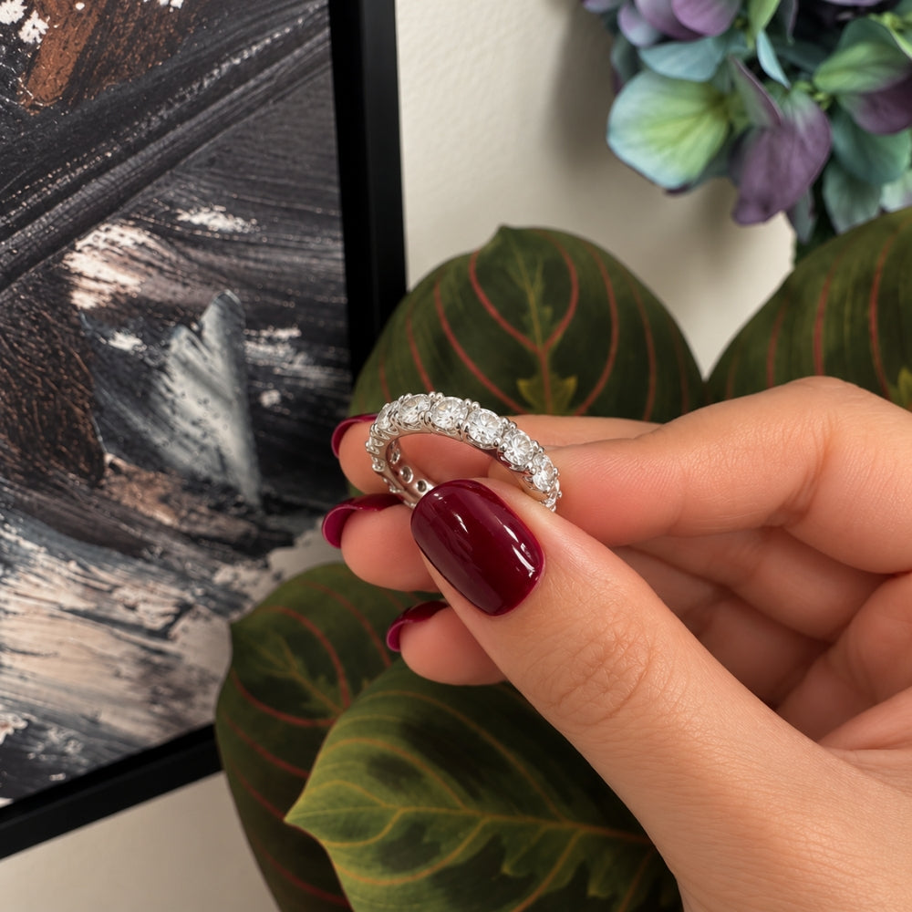 Close-up of Marla Jewellery Moissanite Eternity Ring held by a model with glossy burgundy nails, showcasing sparkling round-cut stones and a polished silver setting.