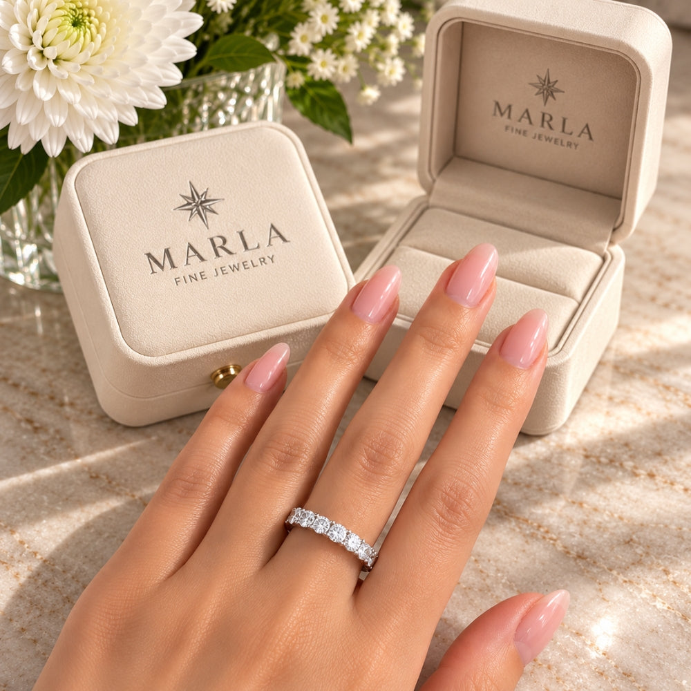Silver Moissanite Eternity Ring by Marla Jewellery worn on a model's hand with pink manicured nails beside luxury cream Marla jewellery gift boxes.