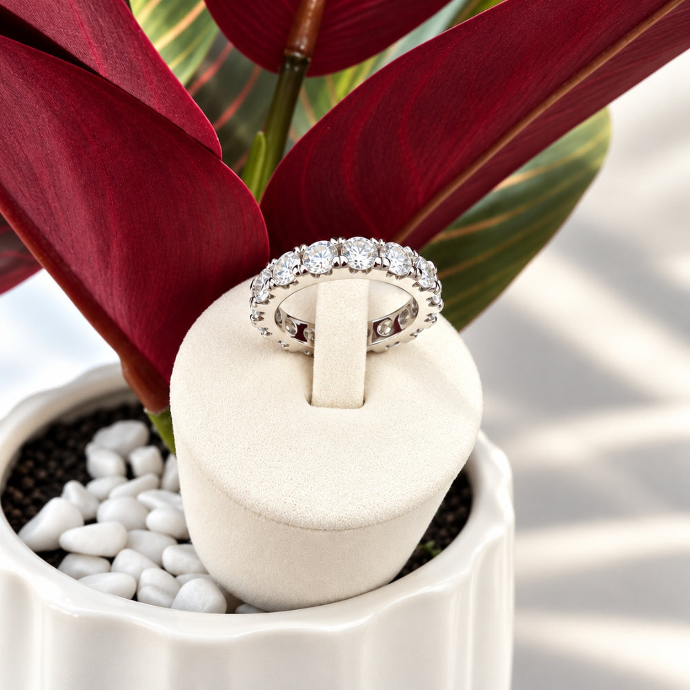 Marla Jewellery silver Moissanite Eternity Ring featuring brilliant round-cut stones on an ivory velvet stand with deep burgundy tropical leaves.
