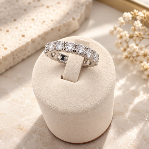 Marla Jewellery Moissanite Eternity Ring in 925 sterling silver, featuring sparkling round-cut stones on an ivory velvet stand with a beige marble background.