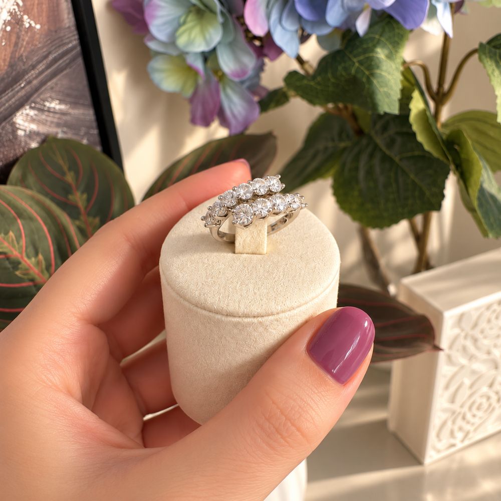 Marla Jewellery silver-tone double-row crystal ring with sparkling round-cut stones, displayed on an ivory velvet stand against pastel flowers.