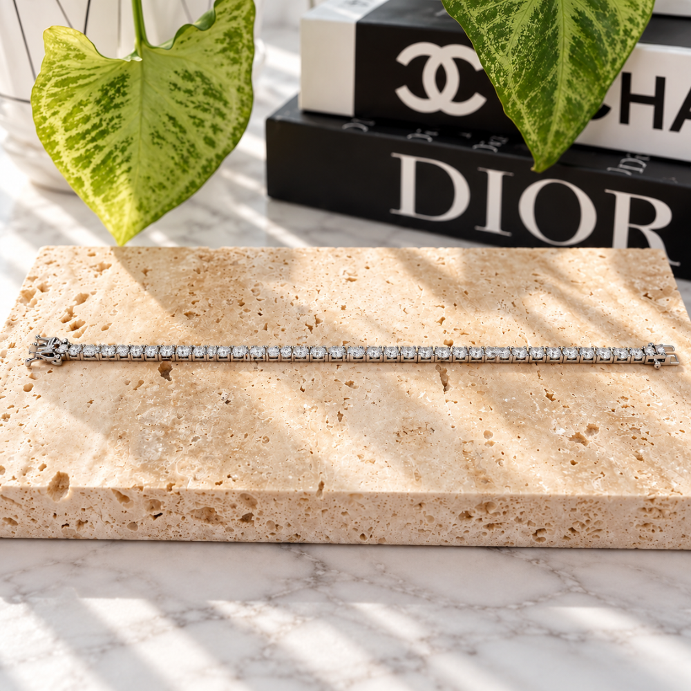 MARLA silver-tone moissanite tennis bracelet featuring a continuous row of sparkling stones on a beige travertine display.