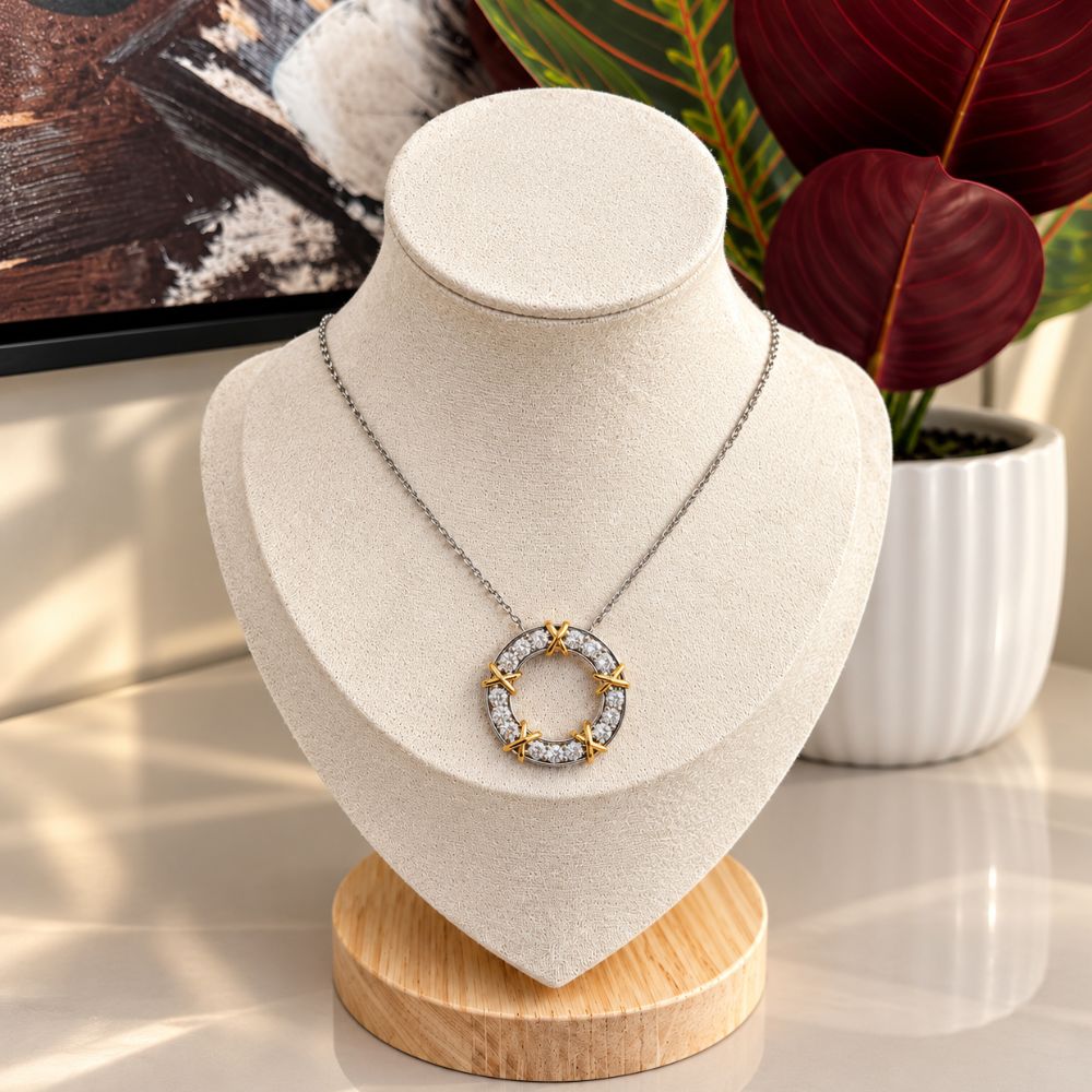 Luxury two-tone diamond circle pendant necklace displayed on an ivory jewellery stand with burgundy tropical leaves in the background.