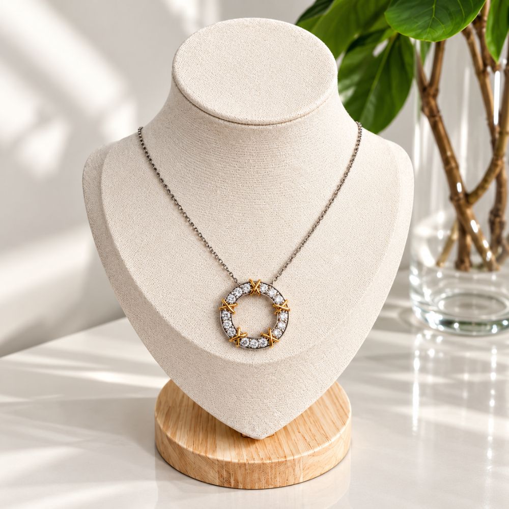 Two-tone diamond circle pendant necklace displayed on a cream linen jewellery bust with natural green foliage in the background.