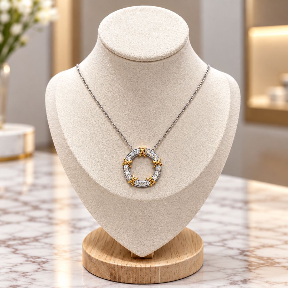 Two-tone diamond circle pendant necklace with gold X accents displayed on an ivory jewellery bust against a luxury marble background.